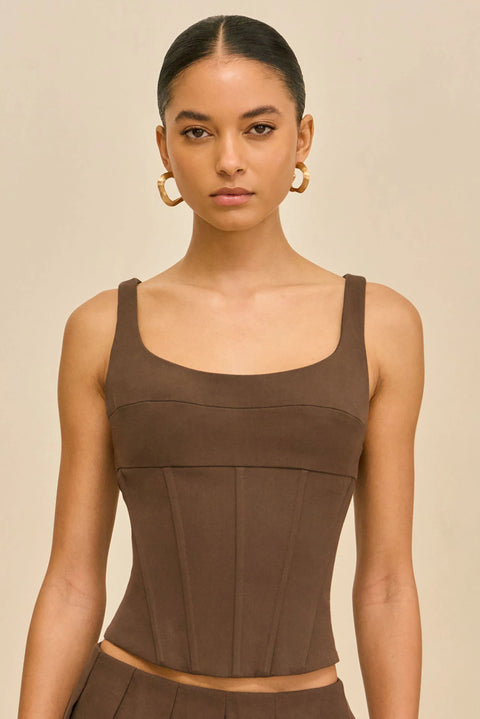 Zoomed in photo of woman wearing a brown sleeveless top and pleated mini skirt on a beige background.