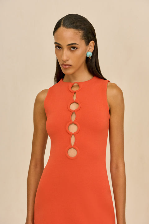Detail shot of woman wearing an orange mini dress with circle cutouts down the chest to the waist on a white background