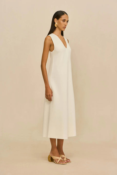 Side view of woman wearing a white sleeveless dress against a beige background