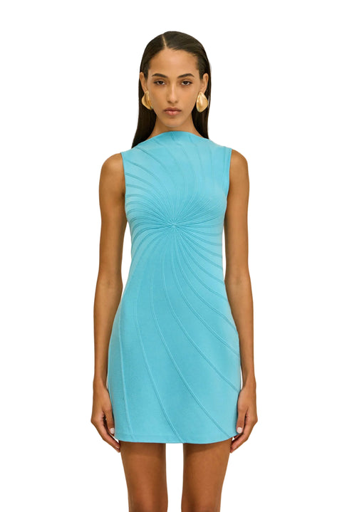 Woman wearing a turquoise mini dress with high neckline against a beige background