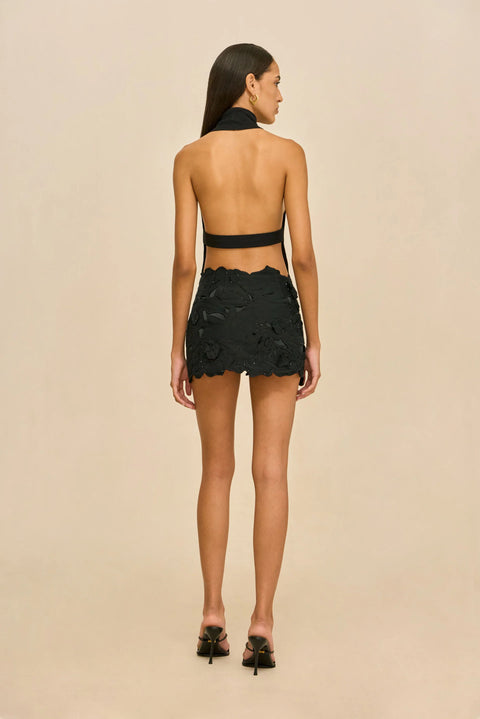 Back-facing shot of woman wearing a black halter top and skirt on a white background