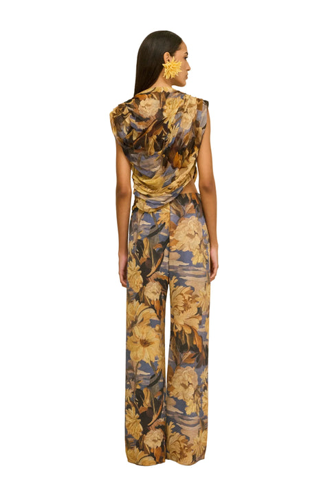 Back-facing shot of woman wearing a floral jumpsuit on a beige background.