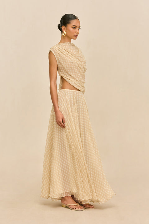 Woman wearing a beige checkered outfit holding a yellow clutch against a white background from the side.