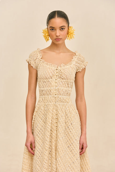 Detail shot of woman wearing a woven beige dress with buttons against a beige background.