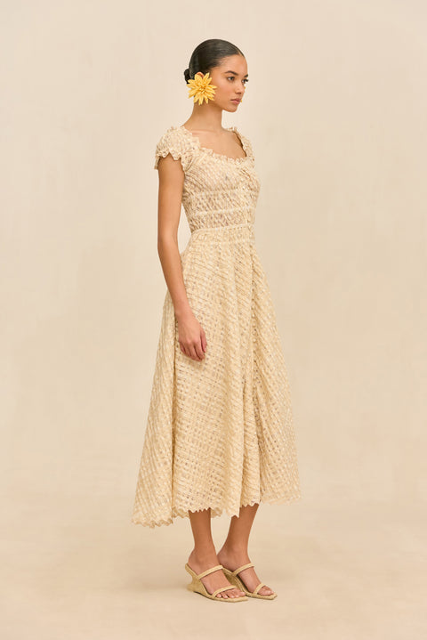 Woman wearing a woven beige dress with buttons against a beige background from the side.