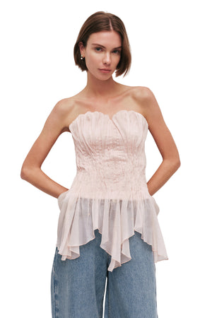 Woman wearing a light pink strapless top and blue jeans against a white background