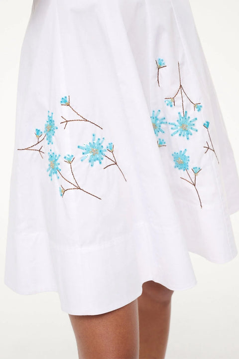 Detail shot of a woman wearing a white mini dress that features blue dandelions beaded and embroidered onto the dress.