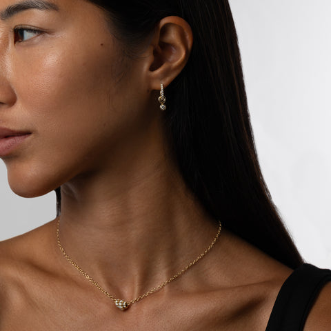 A woman wearing a yellow gold chain necklace that features three yellow gold annulets of differing size, all pave with diamonds. 