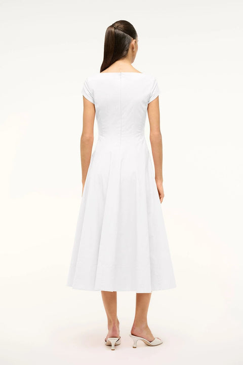 Back view of a woman wearing a white midi dress that features cap sleeves, a square neck, corset styles paneling, and an A-line skirt, paired with white heels. 