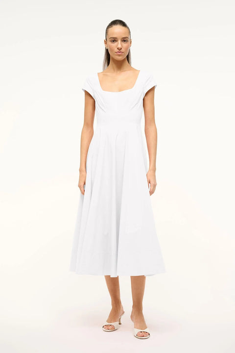 Woman wearing a white midi dress that features cap sleeves, a square neck, corset styles paneling, and an A-line skirt, paired with white heels. 