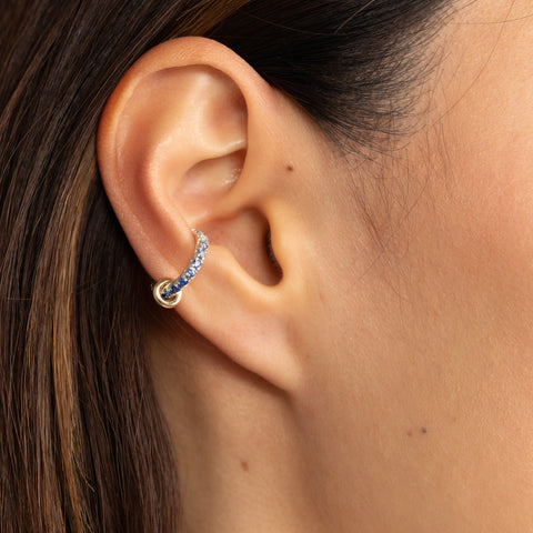 Side-facing woman wearing a sterling silver ear cuff pave with ombre blue sapphires featuring a yellow gold annulet. 