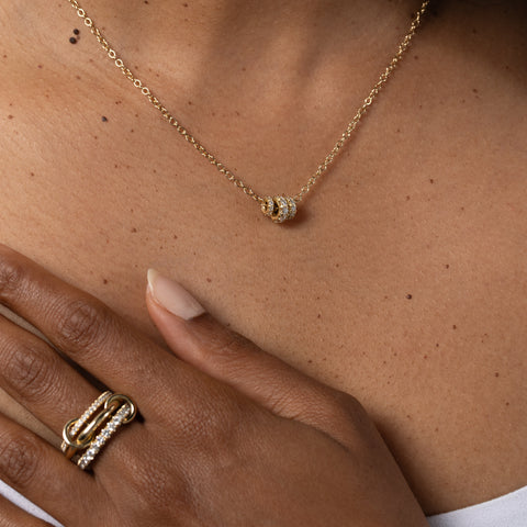 Close up of a woman wearing a yellow gold chain necklace that features three yellow gold annulets of differing size, all pave with diamonds. 