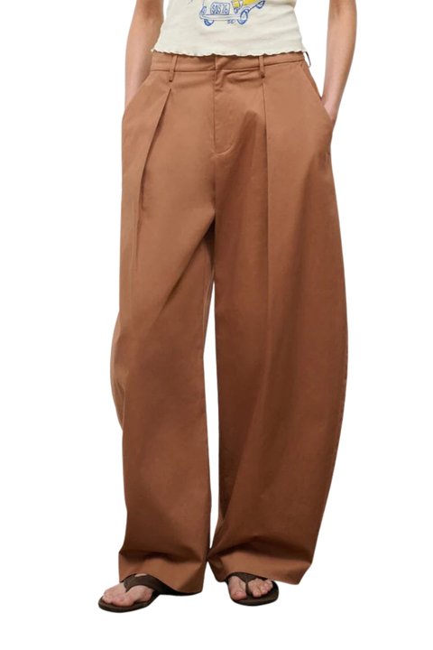 A person wearing wide-leg pleated trousers in a warm brown or rust shade, paired with a cream top and black sandals, shown against a plain white background.