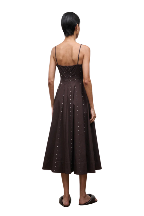Woman wearing a long brown dress with silver studs on a white background back angle