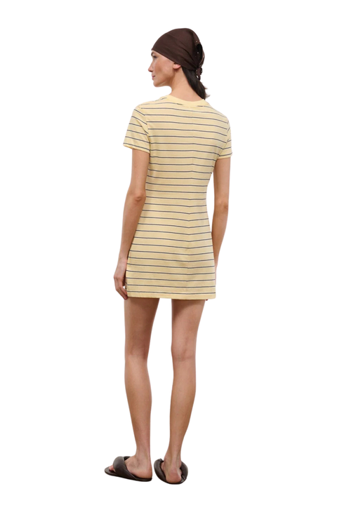 A woman shown from the back wearing a short-sleeve mini dress with thin horizontal yellow stripes on a cream base, paired with a dark brown beanie and black slide sandals, against a plain white background.