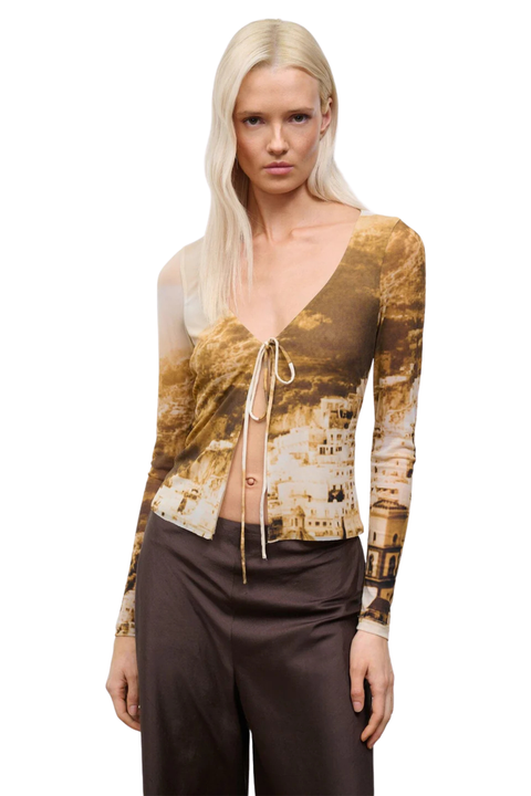 Woman wearing a long-sleeve top with a cityscape print and brown pants on a white background