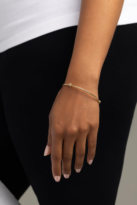 Woman wearing a thin yellow gold bangle that features six yellow gold annulets, one pave with diamonds. 