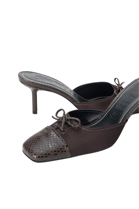 A pair of dark brown mule heels featuring a snakeskin-patterned toe cap and matching bow details, shown against a plain white background.