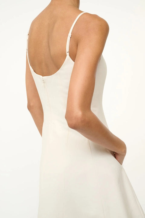 Close up back view of a woman wearing a white mini dress that features a scoop back with a formfitting bodice and circle skirt.