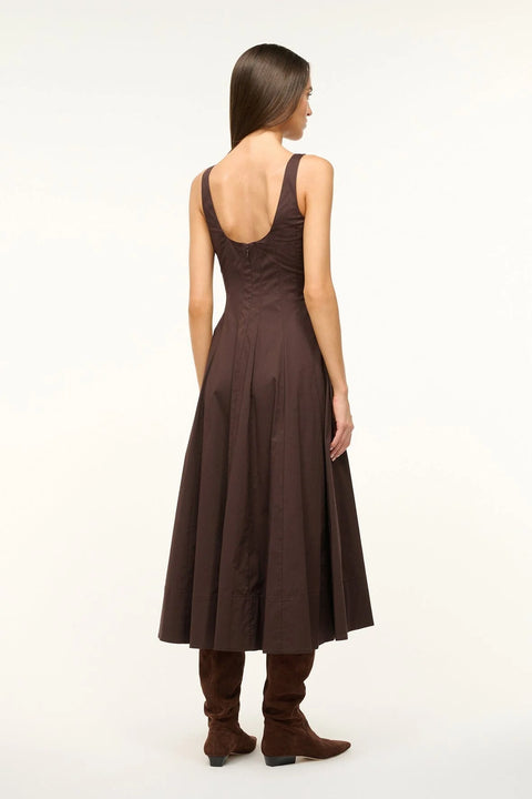 Back view of a woman wearing a brown sleeveless midi dress that features a scoop back, corset-style paneling, and A-line skirt, paired with boots. 