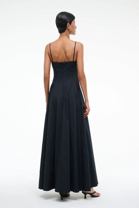 Back-facing woman wearing a black maxi dress that features spaghetti straps, a straight neckline, and corset style pleating, paired with black heels. 