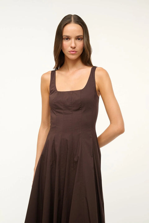 Close up of a woman wearing a brown sleeveless midi dress that features a square neck, corset-style paneling, and A-line skirt. 