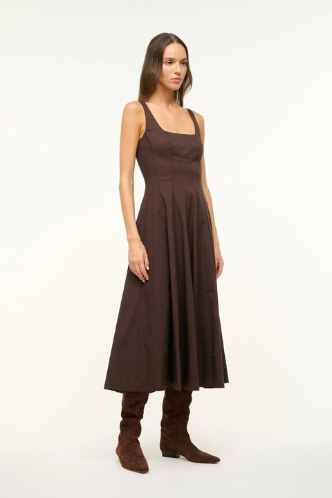 Side view of a woman wearing a brown sleeveless midi dress that features a square neck, corset-style paneling, and A-line skirt, paired with brown boots. 