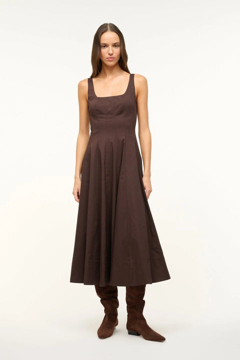 Woman wearing a brown sleeveless midi dress that features a square neck, corset-style paneling, and A-line skirt, paired with boots. 