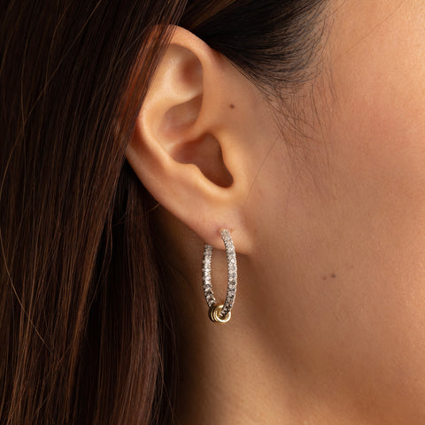 Woman wearing sterling silver hoop earrings pave with ombre white, grey, and black diamonds, featuring three yellow gold annulets. 