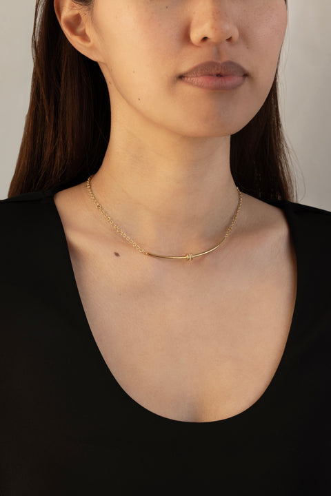 Woman wearing a yellow gold chain necklace that features a yellow gold arced bar with three yellow gold annulets, one pave with diamonds. 