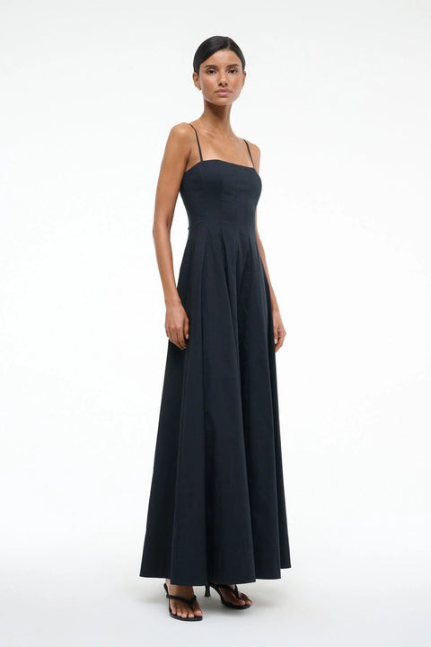 Side-facing woman wearing a black maxi dress that features spaghetti straps, a straight neckline, and corset style pleating, paired with black heels. 