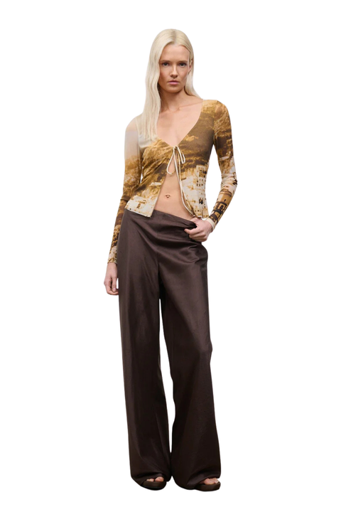 Woman wearing a patterned top and brown pants on a white background