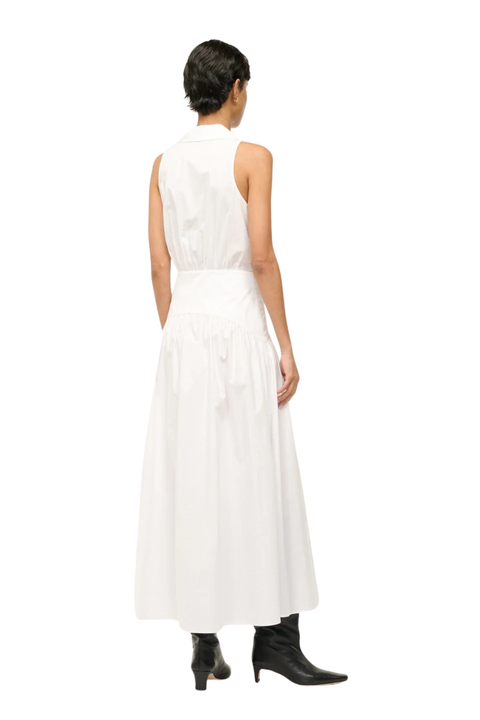 A model viewed from the back wearing a sleeveless white midi dress with a high collar and gathered waist, paired with black ankle boots, against a plain white background.