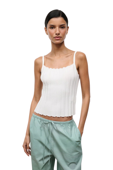 Woman wearing a white ribbed tank top and light green pants on a white background
