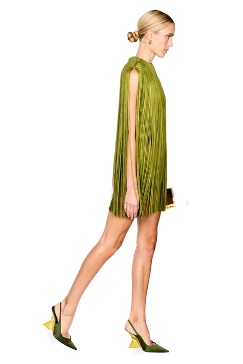 A woman modeling a sleeveless olive green mini dress with a high neckline, paired with matching green slingback heels with yellow heel accents, against a plain white background.
