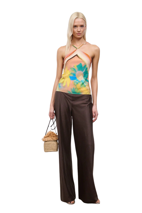 Woman wearing a colorful orange, yellow, and blue sleeveless halter neck top with brown linen pants side