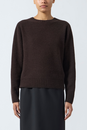 Person wearing a brown crewneck sweater and black skirt on a white background