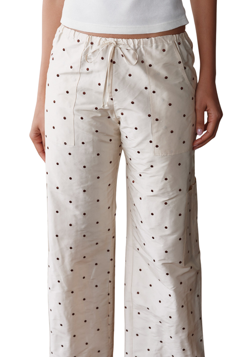 A person wearing cream-colored wide-leg pants with a small black polka dot pattern and a drawstring waistband, shown from the waist down against a plain white background.
