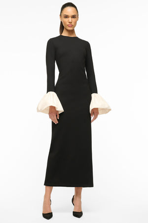 Woman wears black long sleeve maxi dress with voluminous taffeta cuffs.