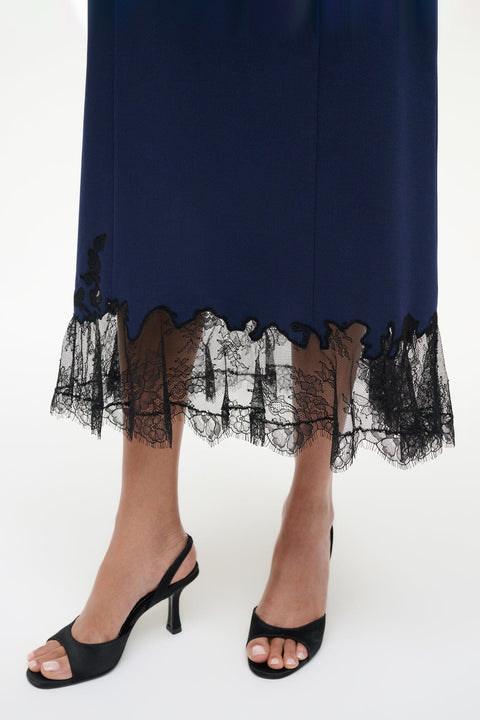 Close up of the bottom of a navy midi dress that features black lace trim along the hem, paired with black slingback kitten heels. 