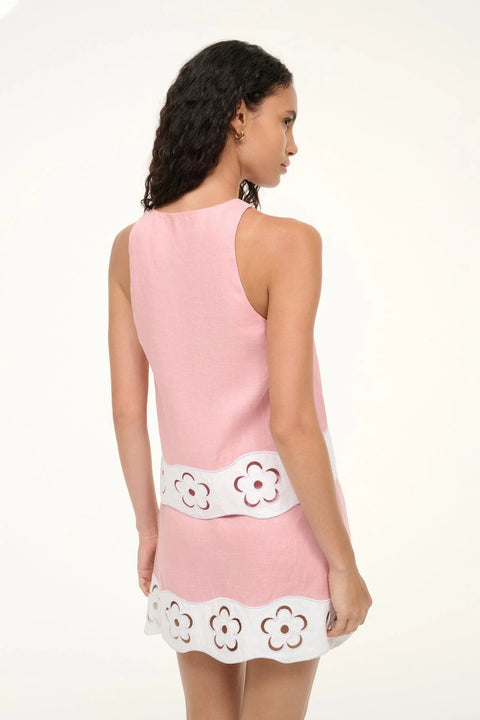 Back view of a woman wearing a pink linen tank top that features white floral cutouts at the bottom hem, worn with a matching skirt. 