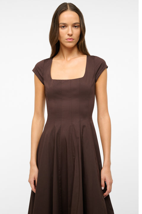 Close up of a woman wearing a brown midi dress that features cap sleeves, a square neck, corset styles paneling, and an A-line skirt.