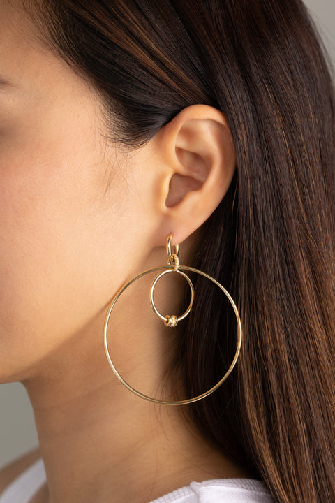 A woman wearing a pair of Spinelli Kilcollin Echo earrings the features a series of different sized yellow gold hoops with yellow gold annulets, some pave with diamonds. 