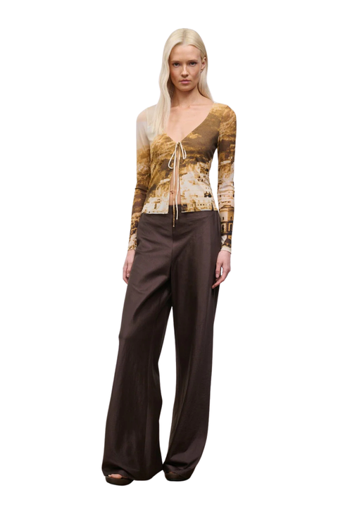 Woman wearing a patterned top and brown pants on a white background