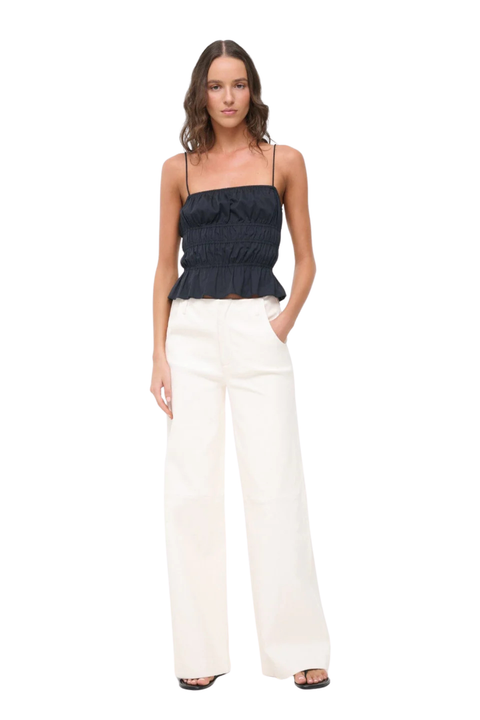 A woman modeling a black strapless ruffled camisole top paired with off-white wide-leg trousers, shown against a plain white background.