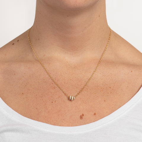 Woman wearing a yellow gold chain necklace that features three yellow gold annulets of differing size, all pave with diamonds. 