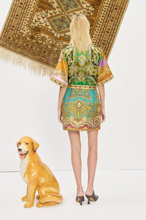 Back-facing woman wearing a multicolor, printed, mini shirtdress that features a point collar and self-tie belt, paired with brown mules. 