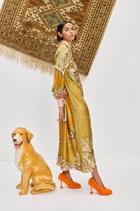 Side-facing woman wearing a multicolor, midi length, long sleeve shirt dress that features a point collar, balloon sleeves, and a self tie belt, paired with orange heels. 