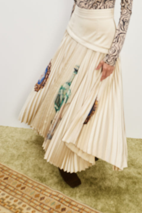 Action shot of a woman twirling in a cream pleated midi skirt that has a fitted corset-style waist and colorful icons printed on the skirt. 