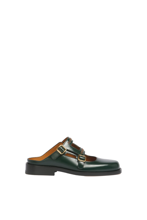 Green leather backless loafer shoe with buckles on a beige background